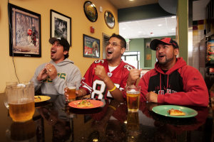 Three guys with beer and pizza watching an exciting sports game on the restaurant’s big screen