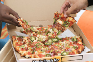 Two customers grab slices from a large, delicious pizza